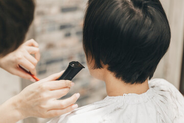 hairdresser makes a haircut to a woman in the salon. The hairdresser cuts wet hair, combing with a comb. client with short hair. back view