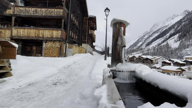 The small village of Blatten in the L&ouml;tschental valley in Switzerland. Snowy village in the Swiss mountains with lots of snow and ice. The fountain is frozen over
