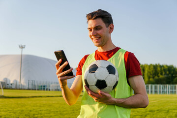 Portrait of young smiling man football player holding soccer ball and using smartphone © glebcallfives