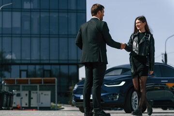 Businessman standing and making handshake with woman near electric car