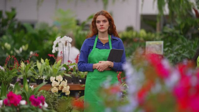 Candid pensive female Florist employee standing inside flower shop. Contemplative woman daydreaming at plant retail store