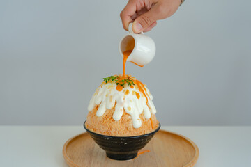 Japanese shaved ice dessert , Hand pouring sweet Thai tea sauce on whipping cream. Served with milk tea kakigori bingsu topped with almond slide condensed milk. Traditional summer dessert in Japan.