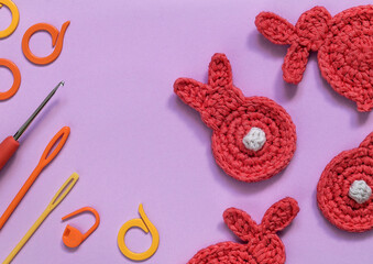Crochet accessories and crochet red rabbit on a violet background. Top view. Copy space.