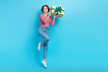 Full size portrait of cheerful overjoyed girl arms hold giftbox jumping isolated on blue color...