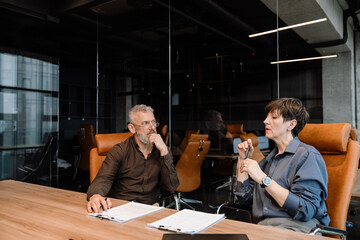 Pensive mature colleagues talking about contract in office