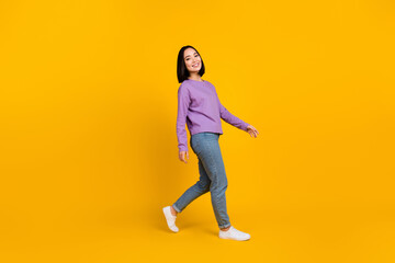 Full length photo of satisfied nice woman wear purple shirt jeans shoes walking to empty space isolated on yellow color background