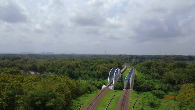 Aerial drone shot of train running on the rail and cross the metal bridge with view of rural landscape, Indonesia. Transportation concept  - 4K drone footage