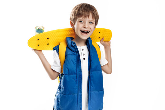 Smiling blonde boy holding yellow longboard and looking away on white background.