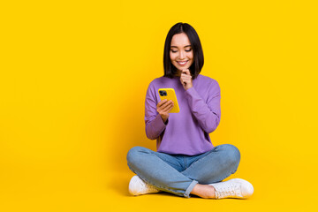 Photo of shiny thoughtful woman wear violet shirt arm hand chin reading modern gadget empty space isolated yellow color background
