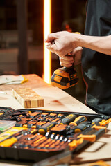 over a workbench with a bench tool, the hands of a worker tighten the drill into the chuck of an electric drill-driver with a replaceable battery