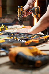 different tools are on the workbench. focus on the hands of a worker who drills with a drill driver...