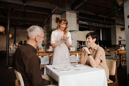 Funny young blonde waitress writes down order of elderly couple in cafe