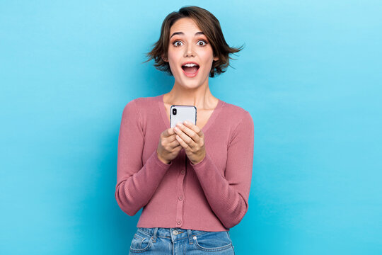 Portrait of excited impressed girl short hairdo wear pink cardigan astonished staring hold smartphone isolated on blue color background