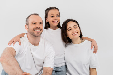 stylish family in white t-shirts looking away while posing together on grey background, International child protection day, preteen daughter hugging happy parents