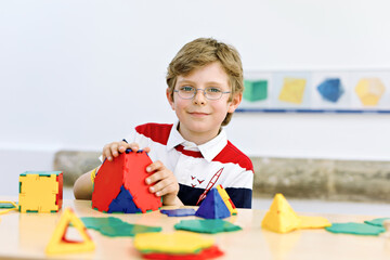 Happy kid boy with glasses having fun with building and creating geometric figures, learning...