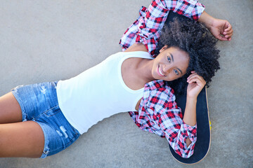 young african american girl smiling lying on the floor with her head resting on her skateboard