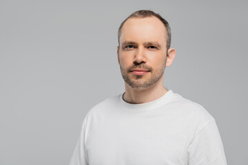 unshaved man with bristle standing in white t-shirt and looking at camera while posing isolated on...