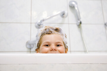 Cute child with shampoo foam and bubbles on hair taking bath. Portrait of happy smiling preschool...