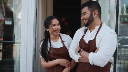 Laughing multinational business owners look into camera near entrance to cafe