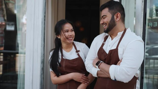 Laughing multinational business owners look into camera near entrance to cafe