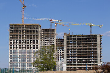 Construction site. Reinforced concrete frames of multi-storey buildings and construction cranes. Against the background of the blue sky.