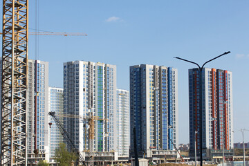 Fototapeta premium Construction site. Reinforced concrete frames of multi-storey buildings and construction cranes. The final stage of construction. Against the background of the blue sky.