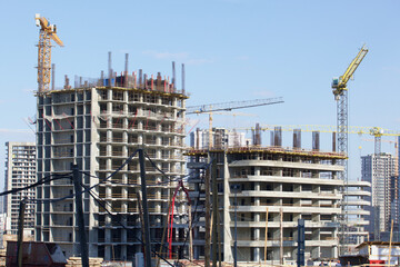 Construction site. Reinforced concrete frames of multi-storey buildings and construction cranes. Against the background of the blue sky.