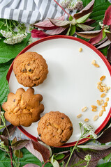 Muffins and peanuts on a ceramic plate, with green and red plant leaves and wild flowers on cotton tablecloth. Mock up. Template for recipes or food menu