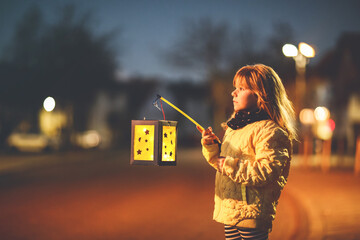 Little preschool kid girl holding selfmade traditional lanterns with candle for St. Martin...