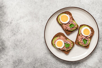 Tuna toast. Open Sandwiches with tuna, rye bread, boiled egg, avocado., light stone background. Top view, flat lay, copy space. Mediterranean food.