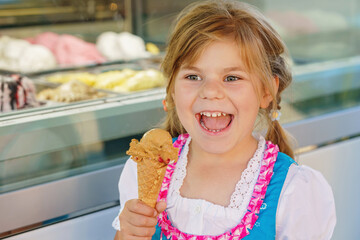 Little preschool girl eating sweet ice cream in waffle cone on sunny summer day. Happy toddler...