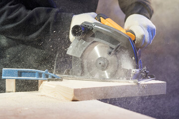 a wooden beam, rounded up with a clamp, is sawn by the hands of a worker using a circular saw....