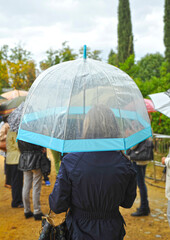 Woman with transparent umbrella on a rainy autumn day. Group of people with umbrellas in the rain in a park