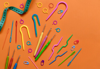 A set of different knitting accessories on an orange background. Bright colorful neddles, crochet hooks, markers, measuring tape. Copy space.