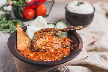 Bebek goreng sambal gami or spicy fried duck is Traditional food from Indonesia. served on plate with a bowl of rice and vegetables. Isolated gray background