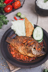 Gurami goreng sambal gami or spicy fried gourami is Traditional food from Indonesia. served on plate with a bowl of rice and vegetables. Isolated gray background