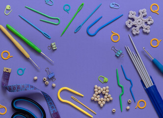 Purple background with knitting and crocheting accessories. Knitting needles, crochet hooks, markers, scissors, measuring tape. Copy space. Top view.