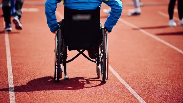A disabled athlete, a man with leg defects, rides in a wheelchair down the stadium street, dressed in sportswear. Former athlete