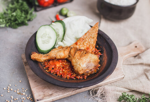 Ayam sambal gami or spicy fried chicken is Traditional food from Indonesia. served on plate with a bowl of rice and vegetables. Isolated gray background