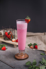 Glass of fresh strawberry milkshake, smoothie and fresh strawberries on dark and wooden background. Healthy food and drink concept.