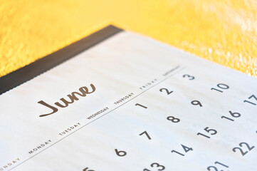 Close up of a simple calendar showing the month of June page with days of the week in English and large numbers on a gold background with shallow depth of field.