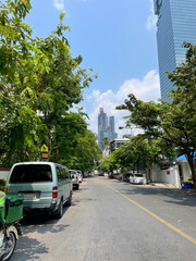 Bangkok city, narrow street with parked transport. Urban skyscrapers, green trees, blue sky with...