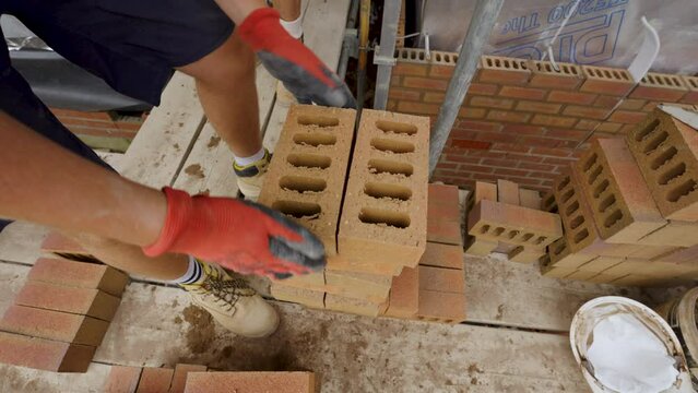 UK - a bricklayer picks up a brick and spins it in the air before adding it back to the stack