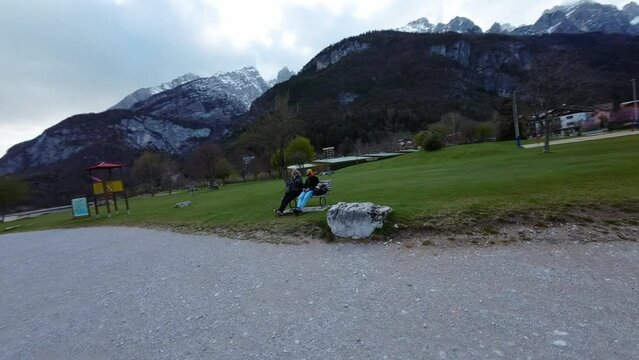 People Sitting On Bench Facing The Beach In Lake Molveno, Trento, Italy. - aerial FPV