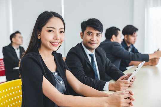 A young businessman sits at the lecture and looks at the camera in a friendly manner.