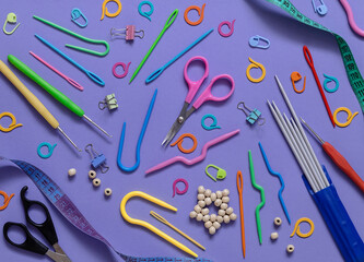 Purple background with knitting and crocheting accessories. Knitting needles, crochet hooks, markers, scissors, measuring tape.