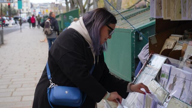 Paris, France - 3 May 2023. Side view of young woman purchases French newspaper from newsstand. Female buying at press kiosk French newspaper. Political, social economic and sport newspapers