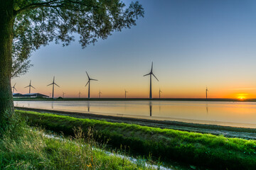 Wind turbines on the dike and in the water at sunset
