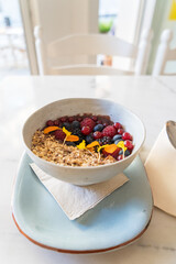 Vertical photo of a typical brazilian açaí bowl with cereals, different berries and edible flowers in a cafeteria.
