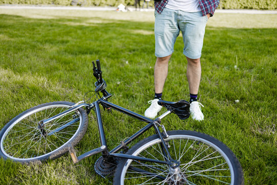 Young man lying on lawn next to bike in summer park. happy person resting after cycling, eyes closed, enjoying silence in nature. Sport, outdoor activity, fitness concept